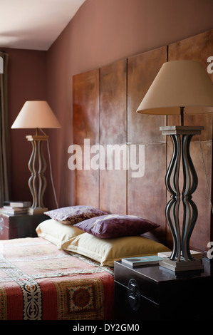 1940 lit en cuir derrière écran flanquée de lampes en fer vintage dans une chambre avec de la peinture murale par Emery & Cie et Banque D'Images