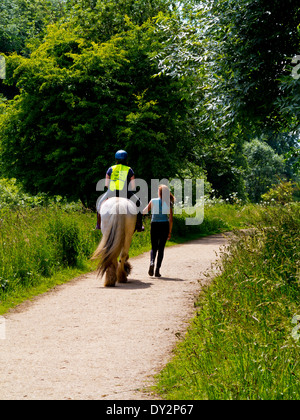 Woman riding un Shire Horse en laisse cours avec instructeur sur un chemin à Creswell Crags dans le Derbyshire, Angleterre, Royaume-Uni Banque D'Images