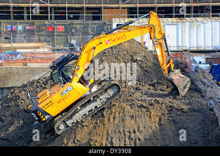J.C. Pelle hydraulique à chenilles Bamford (JCB) : l'acteur et le chargeur en marche remontent jusqu'au sommet du tas de déblais sur le chantier de construction de Londres, Angleterre, Royaume-Uni Banque D'Images