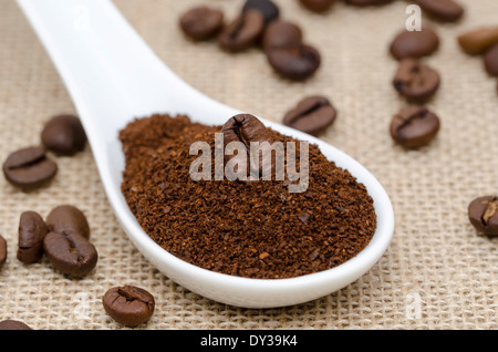 Cuillère en porcelaine blanche avec du café moulu et les grains de café sur une toile Banque D'Images