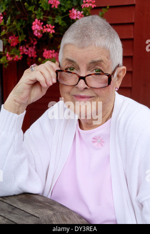 A senior woman avec de courts cheveux gris regarde par-dessus ses lunettes whimsically. Banque D'Images