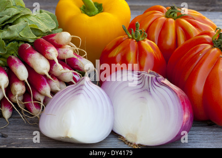 Les tomates Coeur de boeuf, gros oignons rouges et radis frais du marché hebdomadaire sur une vieille table en bois Banque D'Images