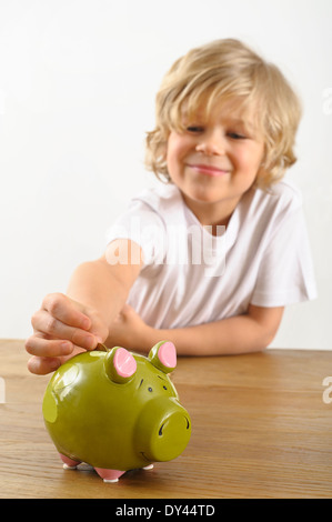 Jeune garçon met une pièce de monnaie dans sa tirelire Banque D'Images