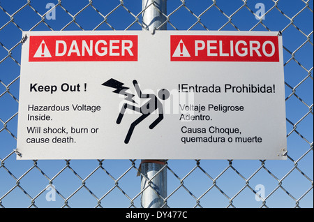 Danger Tension dangereuse à empêcher l'inscription en anglais et espagnol sur une clôture avec ciel bleu Banque D'Images