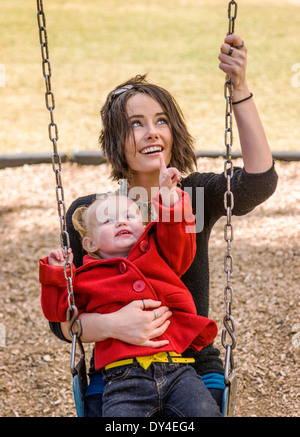 Belle jeune mère jouant avec adorable, jolie petite fille de 16 mois dans le parc de jeux pour enfants balançoires Banque D'Images