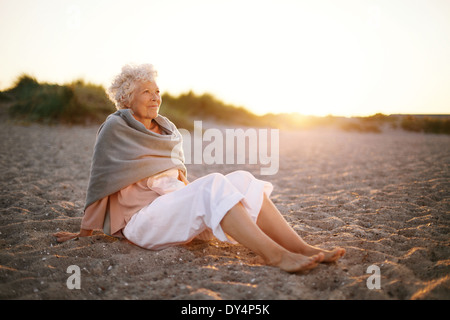 Image de l'ambiance vieille femme assis sur la plage en regardant une vue. Senior woman wearing shawl assis sur la plage. Banque D'Images