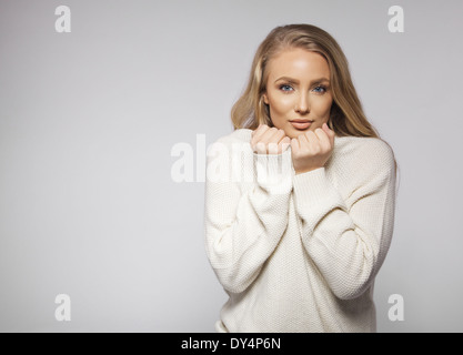 Portrait de jeune et jolie blonde wearing sweater sensations de froid. Cute young female mannequin posant sur fond gris. Banque D'Images