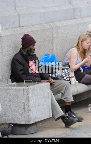 Une personne sans-abri noir barbu assis à Trafalgar Square avec son tous les effets personnels dans un sac en plastique noir à ses côtés, Londres. Banque D'Images