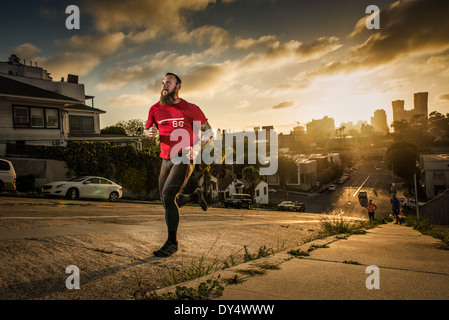 Mid adult male runner et coéquipiers courir vers le haut d'une colline escarpée ville Banque D'Images