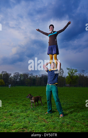 Jeune femme debout sur les épaules de l'homme dans le parc acrobatique, acrobat. Banque D'Images