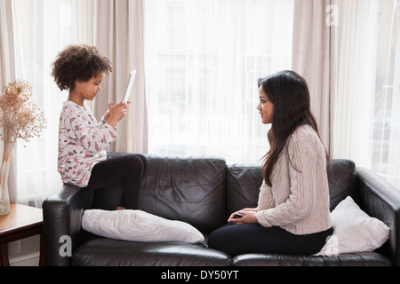 Young Girl taking photograph of teenage sister on digital tablet Banque D'Images