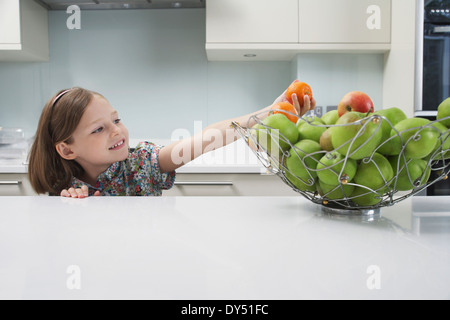 Jeune fille pour atteindre une mandarine à partir de la corbeille de fruits Banque D'Images