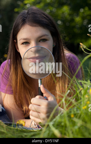 Teenage girl lying in grass brandissant une loupe pour sa bouche Banque D'Images