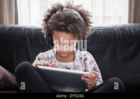 Girl sitting on sofa using digital tablet et écouteurs Banque D'Images