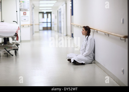 Female doctor sitting cross legged in hospital corridor Banque D'Images