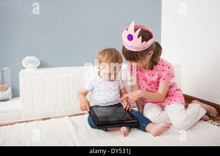 Girl watching over baby boy playing digital tablet Banque D'Images