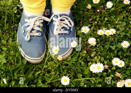 Printemps : teen wearing cars baskets et jeans jaune dans l'herbe parmi les marguerites Banque D'Images