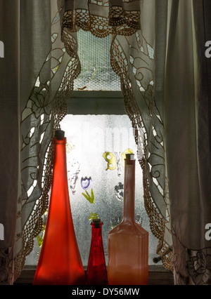 Verser la lumière du soleil dans une fenêtre d'accueil de la banlieue et des rideaux décoratifs en verre rouge sur des flacons de parfum anciens, USA Banque D'Images