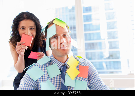 Female office worker couvrant collègue masculin avec sticky notes Banque D'Images