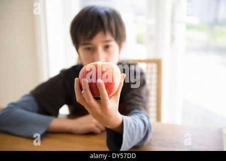 Garçon assis à table, holding apple en face de lui Banque D'Images