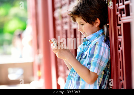 Boy leaning against red door texting on cellphone Banque D'Images