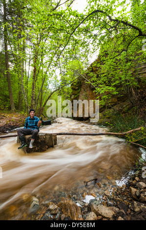 Male hiker assis sur rivière en crue rock, Naramata, British Columbia, Canada Banque D'Images