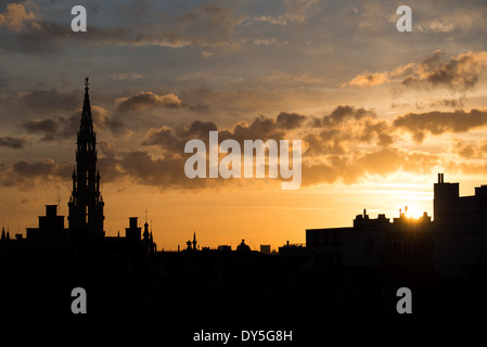 Bruxelles Town Hall Spire Silhouette au coucher du soleil | BRUXELLES, Belgique — la flèche gothique de l'Hôtel de ville perce un coucher de soleil doré sur l'horizon de Bruxelles. La tour de 96 mètres (315 pieds) est couronnée par une figure de girouette dorée représentant Michael, le saint patron de la ville, tuant un dragon - un emblème du XVe siècle qui apparaît toujours sur les armoiries officielles de Bruxelles. Banque D'Images