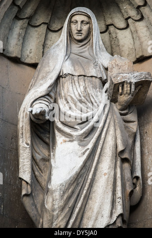 Statue de l'église Saint-Jean-Baptiste Bruxelles Belgique | BRUXELLES, Belgique — Une statue en pierre altérée d'une sainte en roche tenant un livre ouvert orne l'église Saint-Jean-Baptiste au béguinage, une œuvre reflétant la tradition sculpturale baroque flamande du XVIIe siècle. L'église, achevée en 1657, a servi la communauté béguinage de Bruxelles et reste connue pour sa façade baroque et son ornementation. Banque D'Images