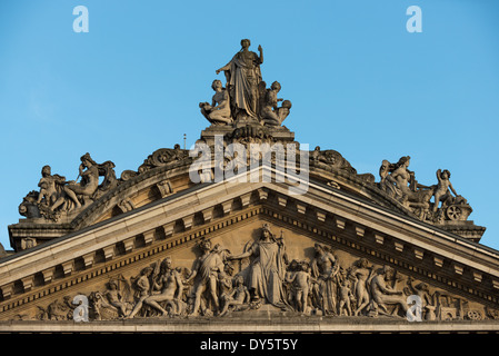 Sculpture du fronton de la Bourse de Bruxelles Bruxelles | BRUXELLES, Belgique — Le fronton couronnant la Bourse de Bruxelles présente un frise allégorique dense de figures drapées et allongées, faisant partie du programme sculptural de la construction du bâtiment entre 1868 et 1873. Des sculpteurs tels que les frères Jacquet, Guillaume de Groot, Albert-Ernest Carrier-Belleuse et un jeune Auguste Rodin ont contribué à la décoration néo-renaissante et du Second Empire. Une figure couronnante et des allégories latérales surmontent la ligne du toit au-dessus du tympan sculpté. Banque D'Images