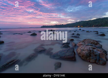 Une longue exposition d'un coucher de soleil rose sur la plage avec des rochers au crépuscule de l'avant-plan, Tangalle, au Sri Lanka, en Asie Banque D'Images