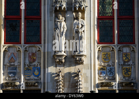 BRUGES, Belgique — des statues médiévales de chevaliers, de membres du clergé et de nobles ornent la façade gothique de l'hôtel de ville de Bruges (Stadhuis), construit en 1376. L'extérieur du bâtiment présente des décorations sculpturales élaborées, y compris des boucliers héraldiques représentant des territoires historiquement gouvernés depuis Bruges. Ces éléments architecturaux démontrent l'importance politique et culturelle médiévale de la ville. Banque D'Images