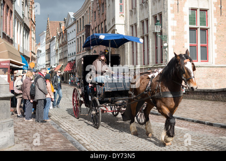 BRUGES, Belgique — les visiteurs explorent les rues médiévales de Bruges en calèche traditionnelle, découvrant le centre-ville historique d'un point de vue unique. Les excursions en calèche offrent un voyage atmosphérique à travers les rues pavées du site classé au patrimoine mondial de l'UNESCO. Cette méthode de visite historique permet aux touristes de découvrir le caractère médiéval préservé de Bruges. Banque D'Images