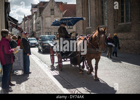 BRUGES, Belgique — les visiteurs explorent les rues médiévales de Bruges en calèche traditionnelle, découvrant le centre-ville historique d'un point de vue unique. Les excursions en calèche offrent un voyage atmosphérique à travers les rues pavées du site classé au patrimoine mondial de l'UNESCO. Cette méthode de visite historique permet aux touristes de découvrir le caractère médiéval préservé de Bruges. Banque D'Images