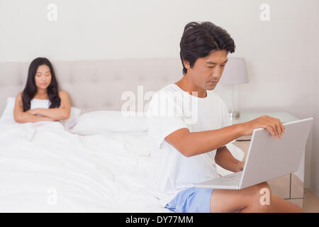 Femme regardant petit ami à l'aide de l'ordinateur portable sur bout de lit Banque D'Images