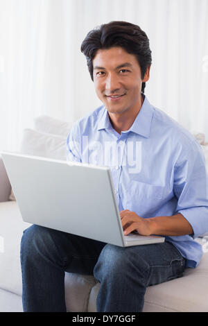 Happy man sitting on sofa using laptop Banque D'Images