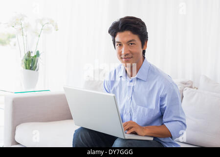 Happy man sitting on sofa using laptop Banque D'Images