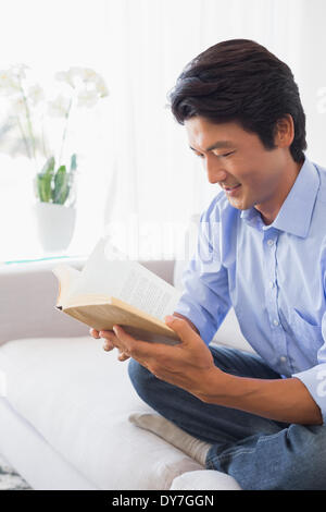 Happy man sitting on couch reading Banque D'Images