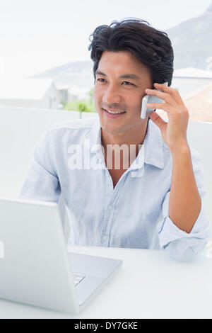 Smiling man en utilisant son ordinateur portable et parlant au téléphone Banque D'Images