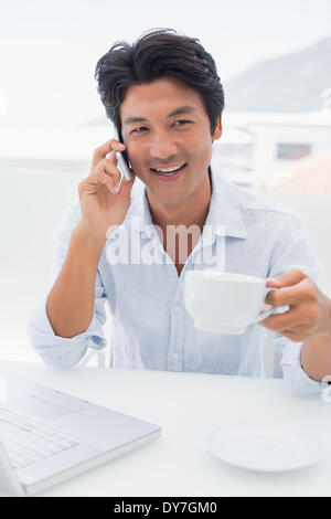 Smiling man having coffee and talking on phone Banque D'Images