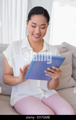 Smiling woman sitting on couch using tablet pc Banque D'Images
