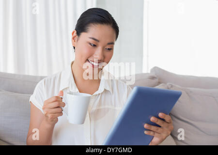 Smiling woman sitting on couch using tablet pc le café Banque D'Images
