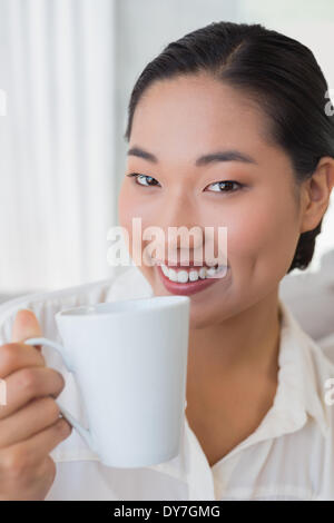 Smiling woman sitting on couch having coffee Banque D'Images