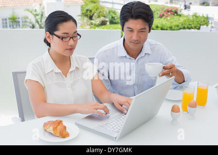 Smiling couple having breakfast together using laptop Banque D'Images