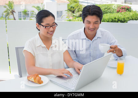 Smiling couple having breakfast together using laptop Banque D'Images