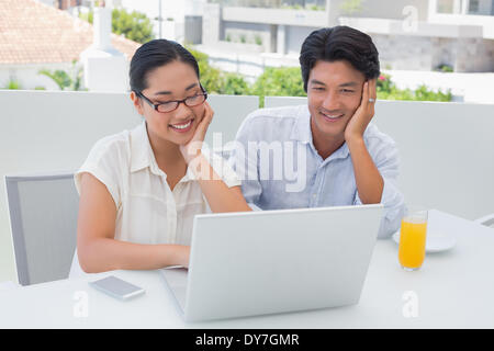 Smiling couple having breakfast together using laptop Banque D'Images