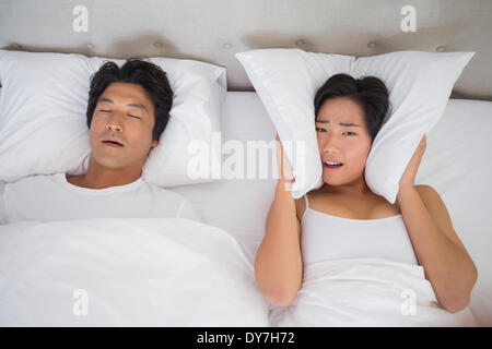 Femme ennuyés couvrant ses oreilles avec des oreillers pour bloquer le ronflement Banque D'Images