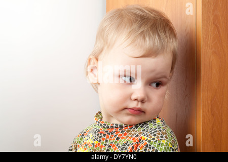 Peu Caucasian baby girl se cacher derrière un placard Banque D'Images