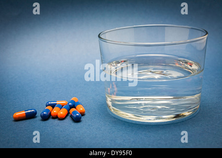 Verre d'eau et des pilules isolé sur blue Banque D'Images