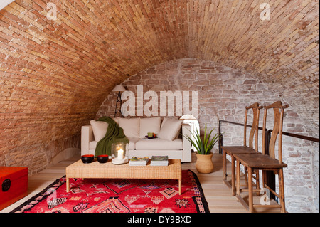 Les murs voûtés en pierre dans l'espace mezzanine avec canapé-lit blanc, table basse en osier et rouge vif tapis ethniques Banque D'Images