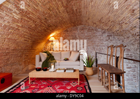 Les murs voûtés en pierre dans l'espace mezzanine avec canapé-lit blanc, table basse en osier et rouge vif tapis ethniques Banque D'Images